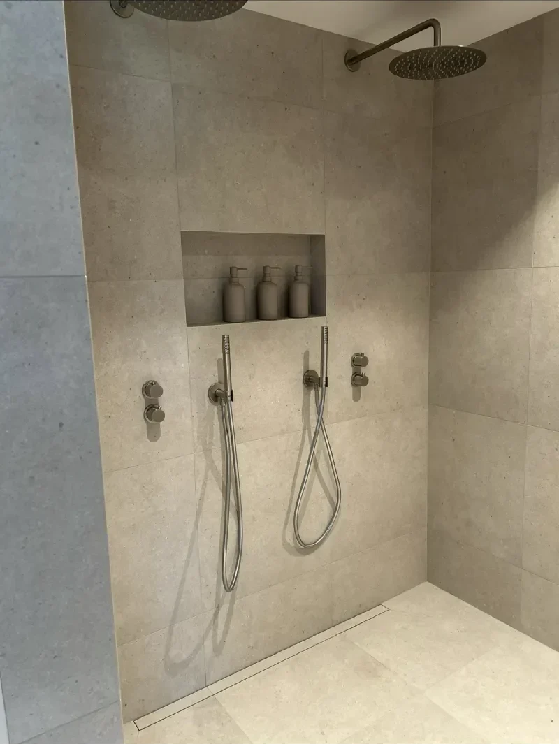 Dubbeldusch med lyxig känsla, stora plattor på golv och vägg, gerad nisch med epoxyfog och golvnära tile-in-brunn, utfört av Mplattsättning AB.