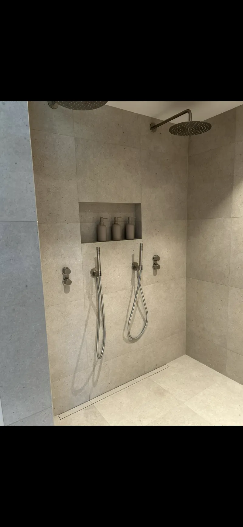 Dubbeldusch med lyxig känsla, stora plattor på golv och vägg, gerad nisch med epoxyfog och golvnära tile-in-brunn, utfört av Mplattsättning AB.
