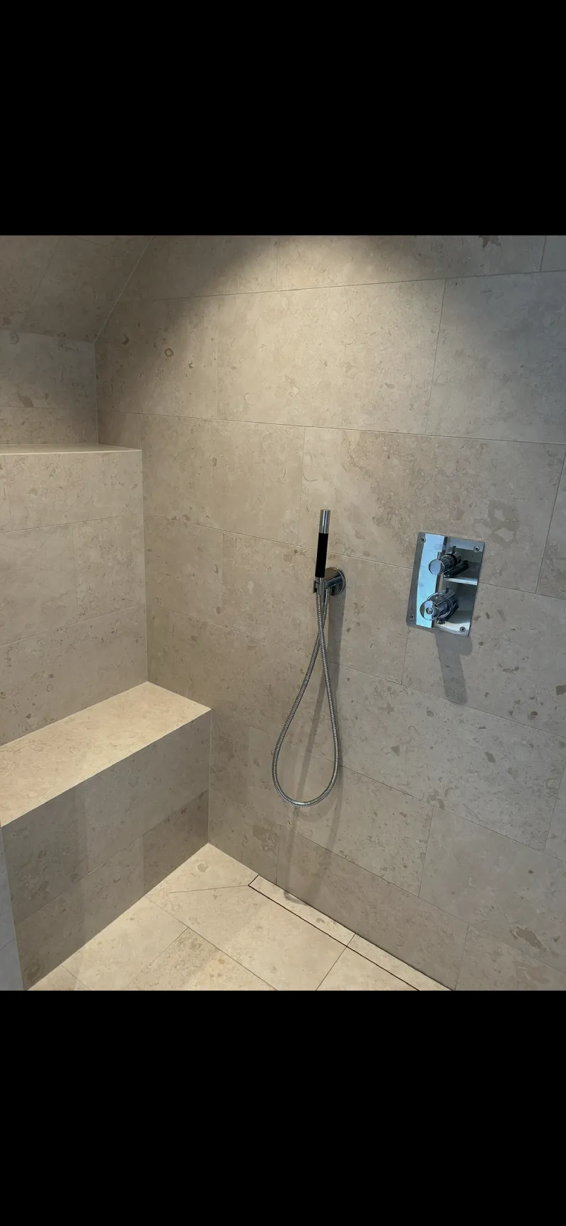 Duschhörna med sittbänk, samma plattor på golv och vägg samt väggnära tile-in-brunn, plattsättning av Mplattsättning AB.