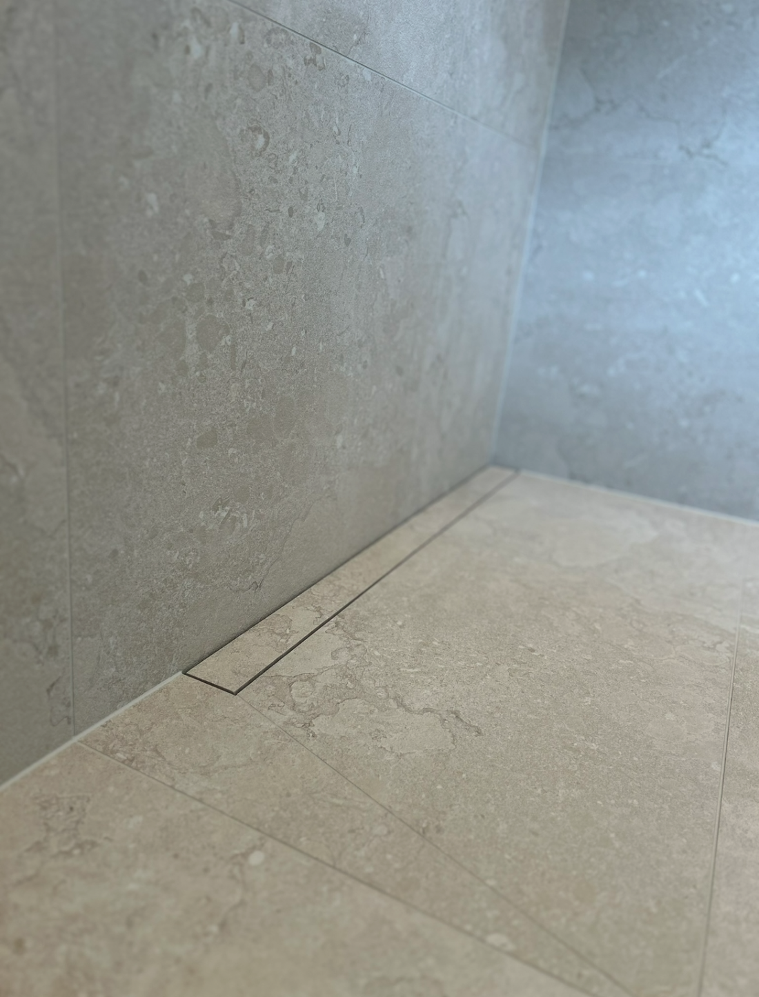 Väggnära tile-in-brunn integrerad i kaklat golv för en modern och diskret badrumslösning utförd av Mplattsättning AB.